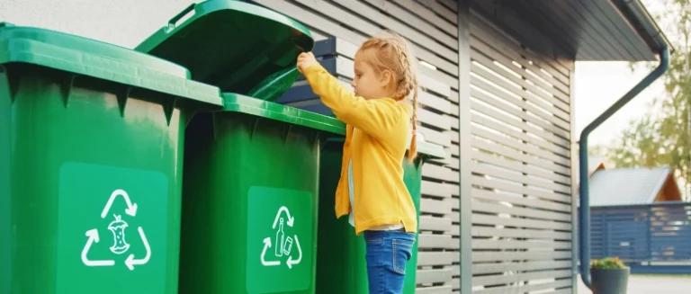 Activity Kits 5 A girl in a yellow cardigan reaches into an open recycling bin.